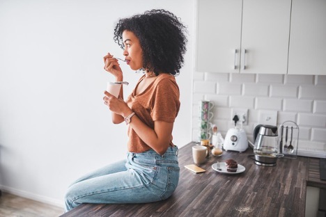 woman-having-a-tub-of-yogurt-in-the-kitchen-probiotics-concept