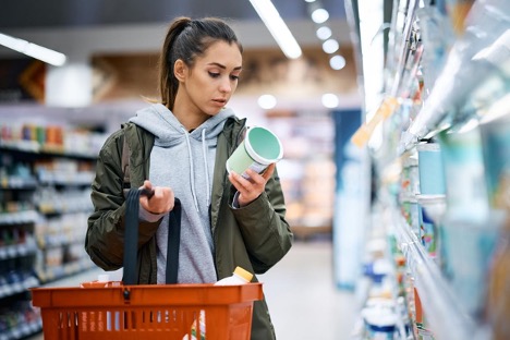 Young woman reading nutrition label and ingredients while buying dairy product in a supermarket