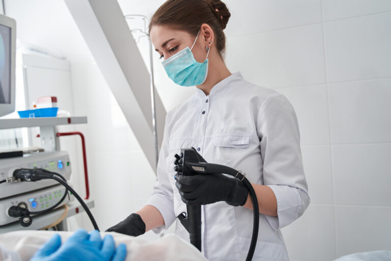 A healthcare professional wearing a surgical mask and gloves is operating a medical device during a procedure.